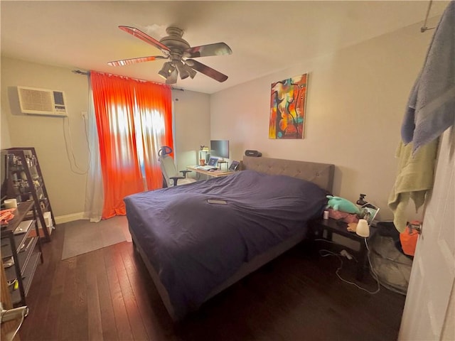 bedroom featuring a wall unit AC, dark wood-style flooring, ceiling fan, and baseboards