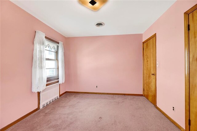 spare room with radiator, baseboards, and light colored carpet