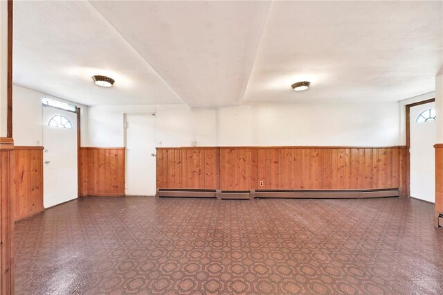 unfurnished room featuring a wainscoted wall, a wealth of natural light, wood walls, and dark floors