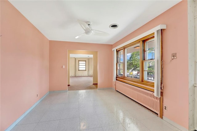 empty room featuring visible vents, baseboards, a ceiling fan, and radiator heating unit