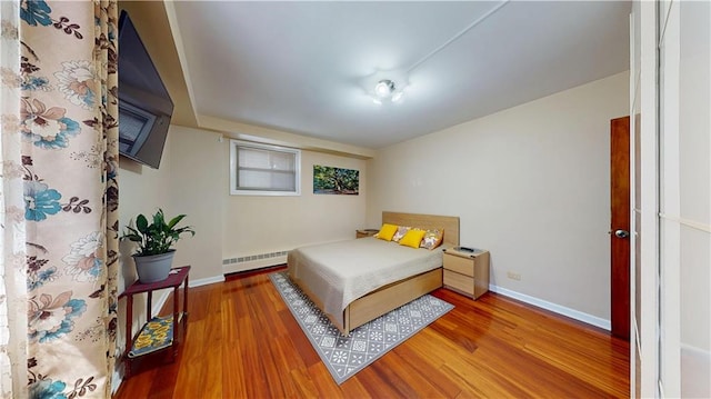 bedroom featuring wood finished floors, baseboards, and a baseboard heating unit