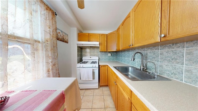 kitchen with a sink, tasteful backsplash, under cabinet range hood, light countertops, and white range with gas stovetop