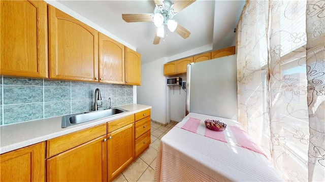 kitchen featuring a sink, tasteful backsplash, freestanding refrigerator, ceiling fan, and light countertops