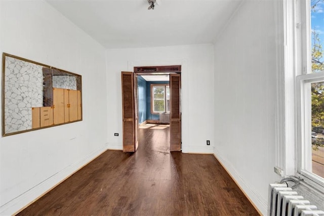 empty room featuring baseboards, radiator heating unit, plenty of natural light, and wood finished floors