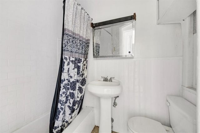bathroom with toilet, shower / tub combo with curtain, and wainscoting