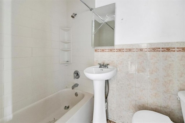 full bath with tile walls, toilet, shower / tub combination, and a sink