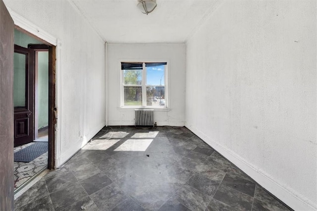spare room featuring radiator, a textured wall, and baseboards
