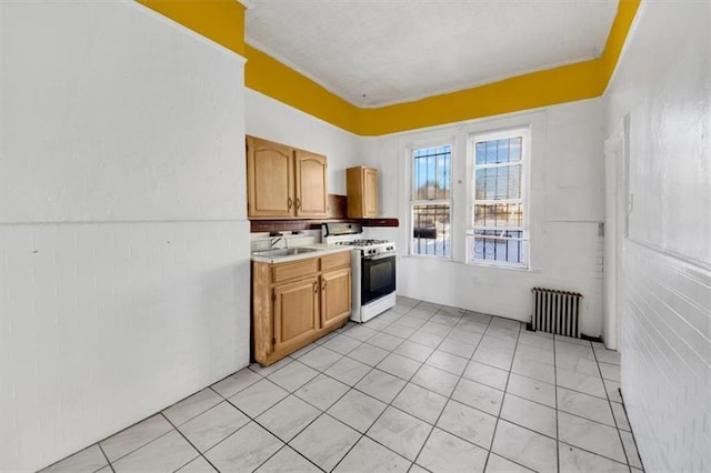 kitchen with light tile patterned floors, radiator, a sink, white gas range oven, and light countertops