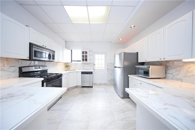 436 76th St, Brooklyn, NY 11209 - kitchen featuring stainless steel appliances, light stone countertops, a paneled ceiling, white cabinets, and backsplash