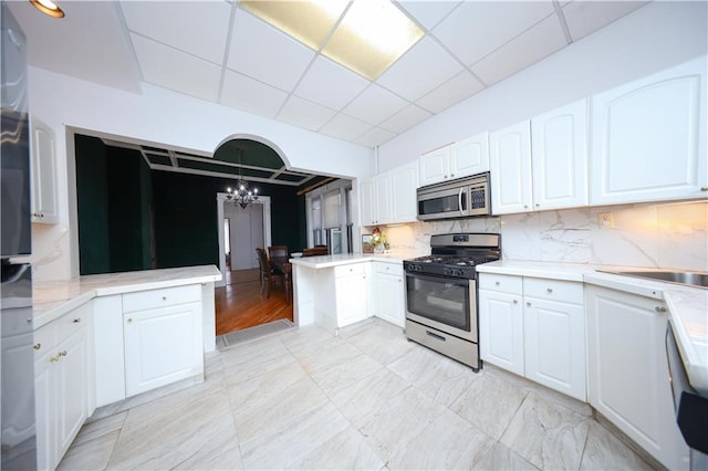 436 76th St, Brooklyn, NY 11209 - kitchen featuring stainless steel appliances, a chandelier, a paneled ceiling, a peninsula, and white cabinetry