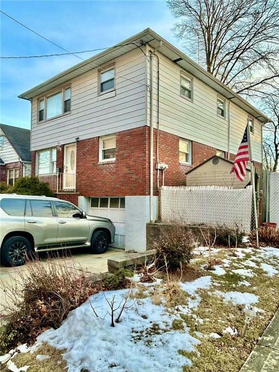 snow covered property with brick siding, fence, and a garage