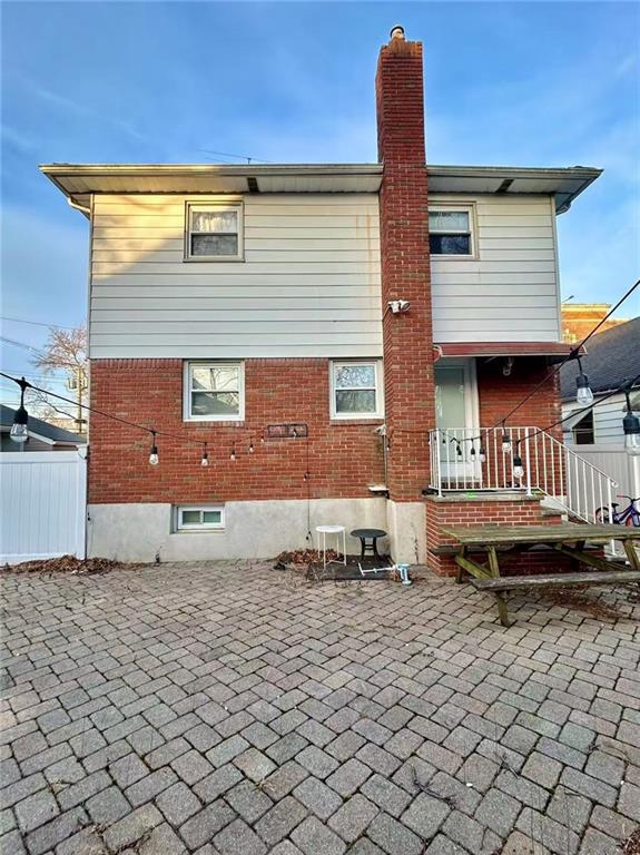 rear view of house with fence, a patio, a chimney, and brick siding