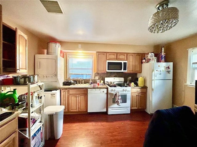 kitchen with stacked washer and clothes dryer, a sink, visible vents, dark wood-style flooring, and white appliances