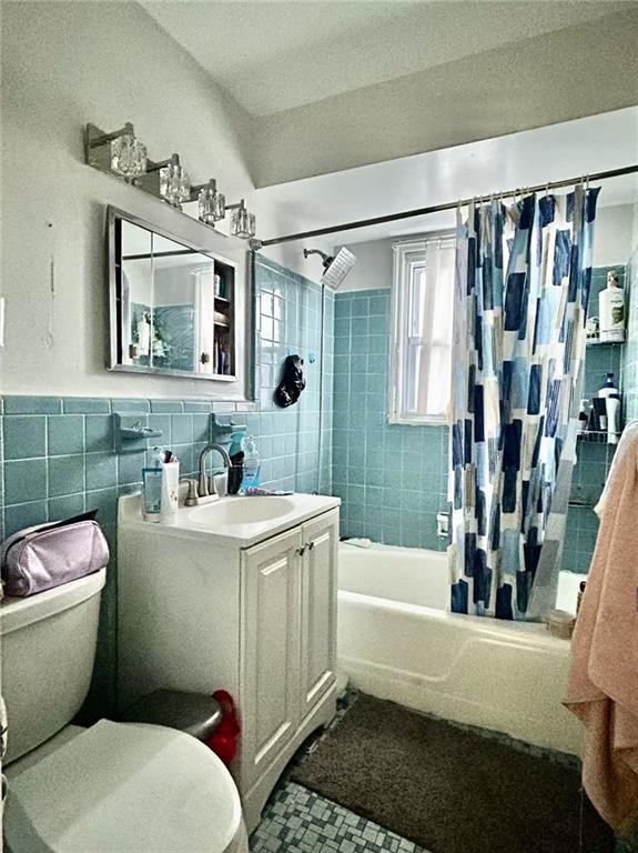 full bath with tile walls, toilet, shower / tub combo with curtain, tile patterned floors, and vanity