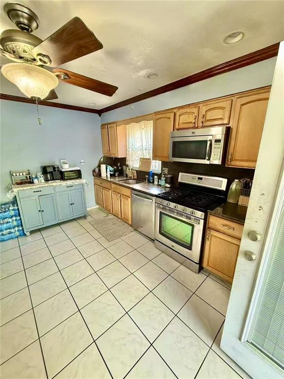 kitchen featuring a sink, stainless steel appliances, crown molding, light tile patterned floors, and dark countertops