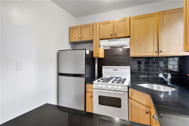 kitchen with under cabinet range hood, white gas stove, freestanding refrigerator, a sink, and backsplash