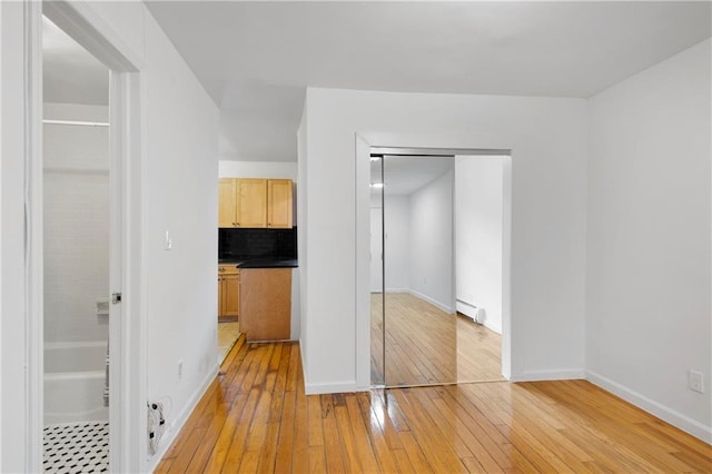 unfurnished bedroom featuring light wood-style flooring, a closet, a baseboard radiator, and baseboards