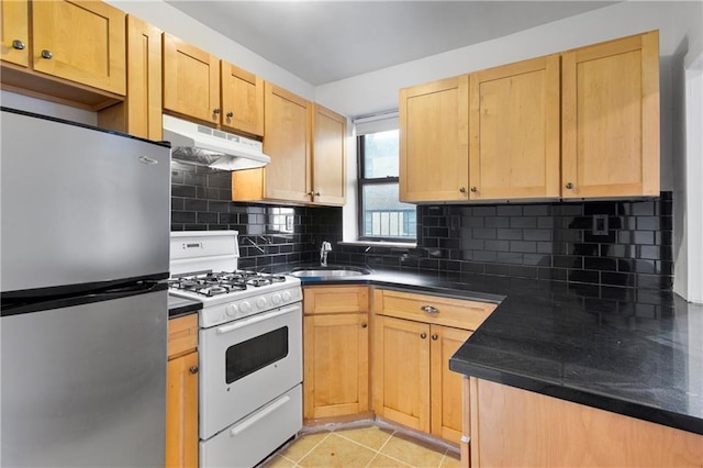 kitchen featuring freestanding refrigerator, white gas stove, under cabinet range hood, a sink, and dark countertops