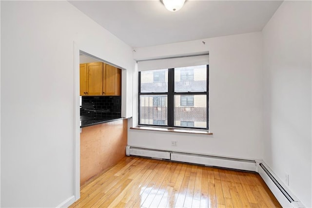 unfurnished room with light wood finished floors and a baseboard heating unit