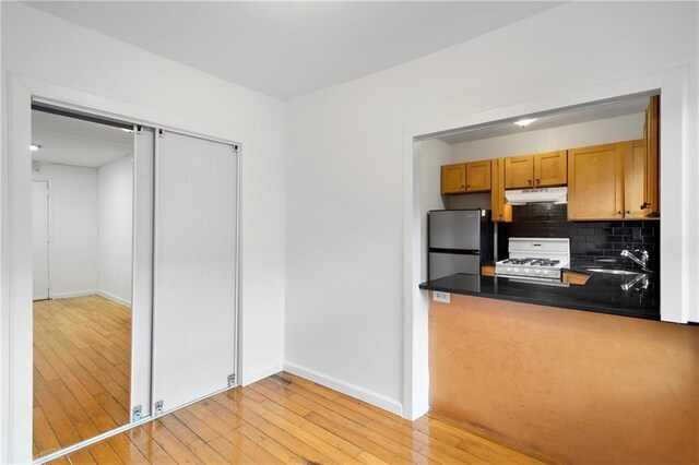 kitchen featuring white gas range, freestanding refrigerator, a sink, dark countertops, and under cabinet range hood
