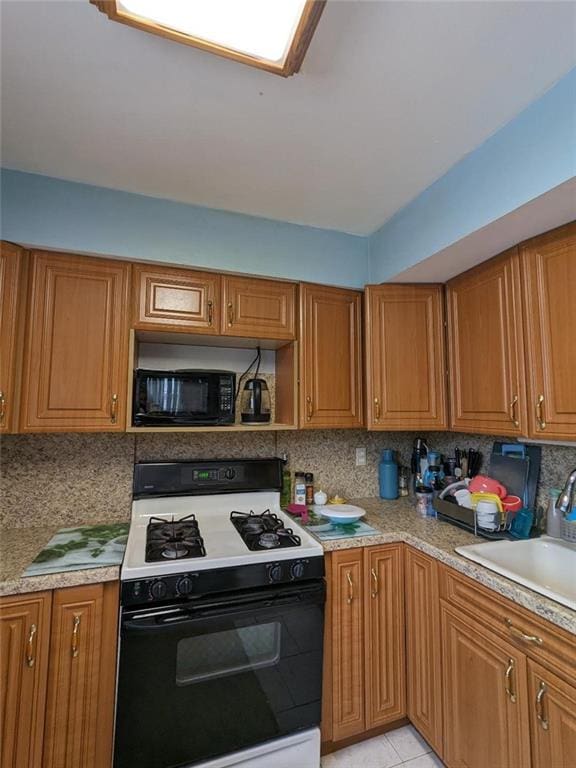 kitchen with brown cabinetry, gas stove, black microwave, decorative backsplash, and light countertops