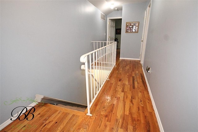 hall with lofted ceiling, baseboards, visible vents, wood finished floors, and an upstairs landing