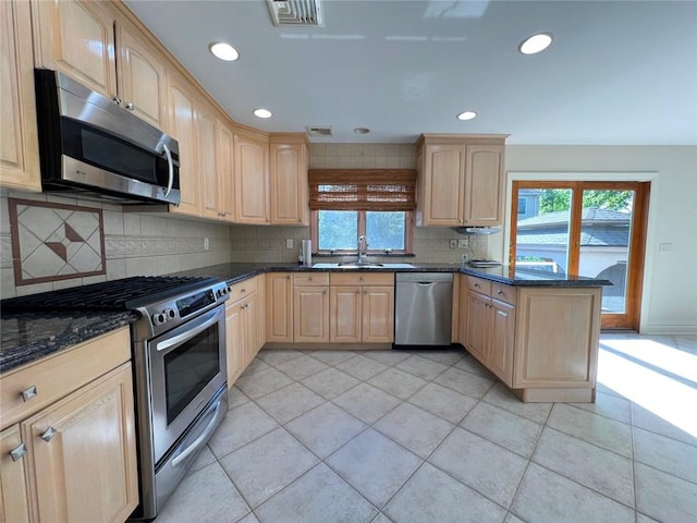 kitchen with appliances with stainless steel finishes, light brown cabinetry, a peninsula, a sink, and tasteful backsplash