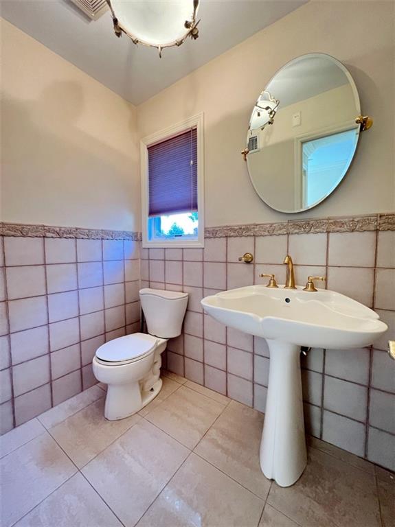 bathroom with tile walls, toilet, a wainscoted wall, and tile patterned floors