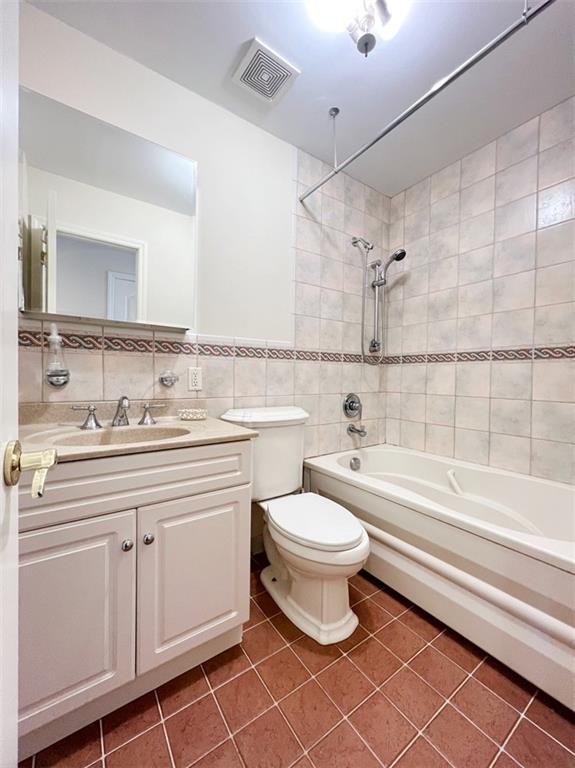 full bathroom with washtub / shower combination, tile patterned floors, toilet, vanity, and tile walls