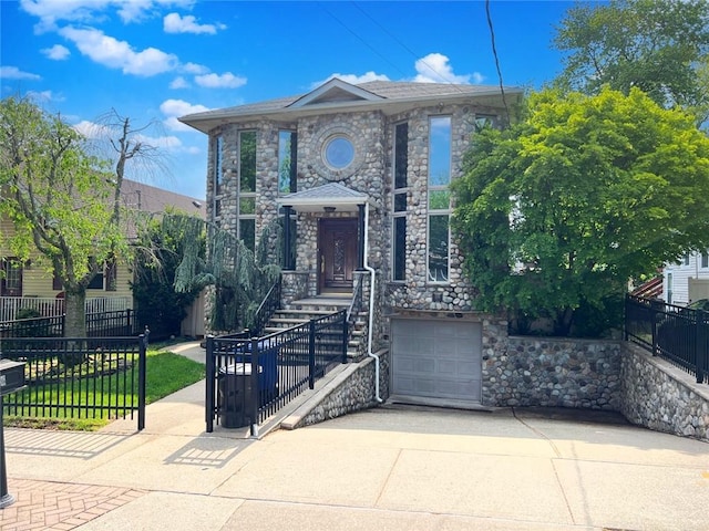view of front of property featuring a fenced front yard, stone siding, a garage, and concrete driveway
