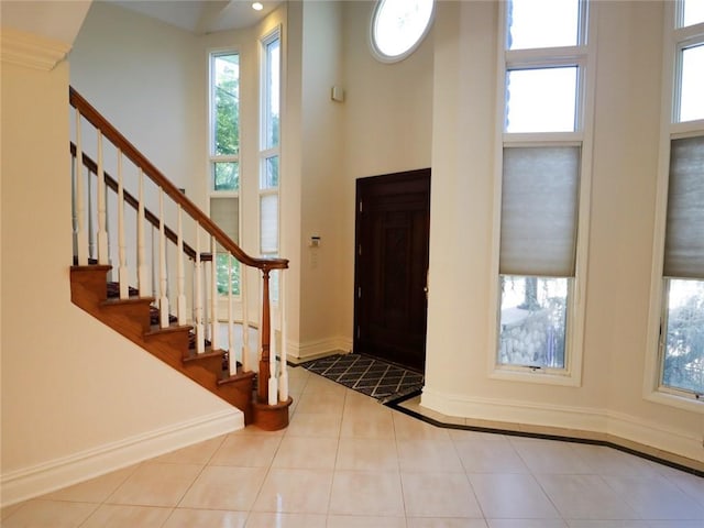 foyer entrance with a towering ceiling, baseboards, tile patterned flooring, stairway, and plenty of natural light