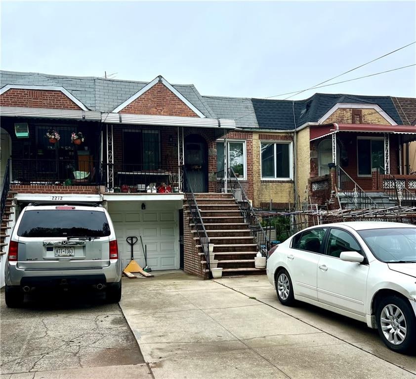 view of property featuring stairway, brick siding, driveway, and a garage