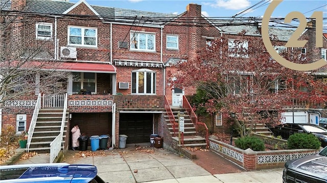 exterior space with stairs, an attached garage, a wall unit AC, and driveway