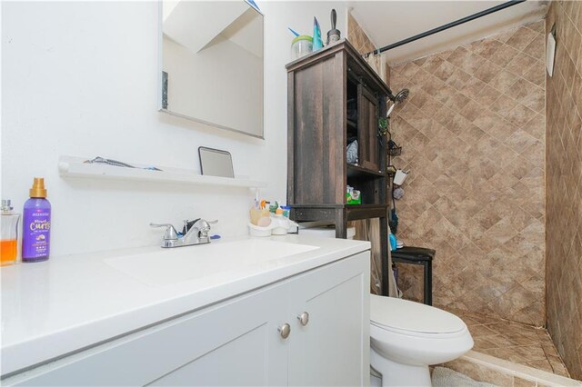 bathroom with a tile shower, toilet, and vanity
