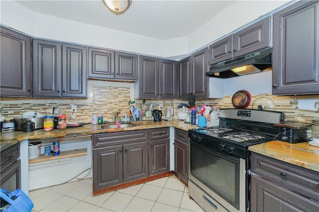 kitchen with stainless steel gas range oven, under cabinet range hood, a sink, decorative backsplash, and light stone counters