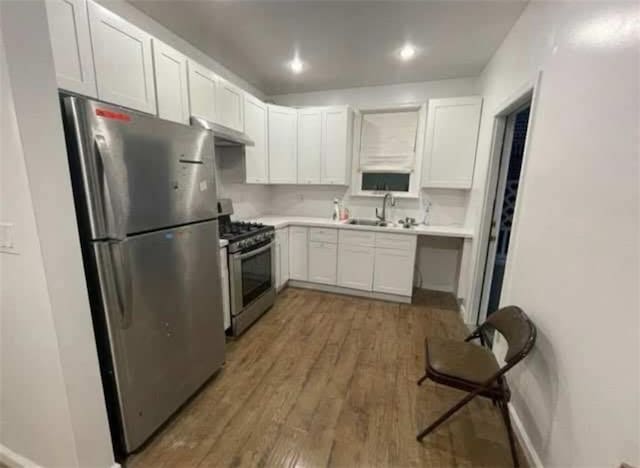 kitchen with appliances with stainless steel finishes, a sink, under cabinet range hood, light countertops, and wood finished floors