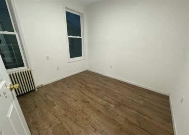 spare room with radiator, wood finished floors, and baseboards