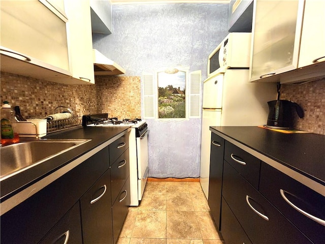 kitchen with white appliances, under cabinet range hood, tasteful backsplash, and dark cabinetry