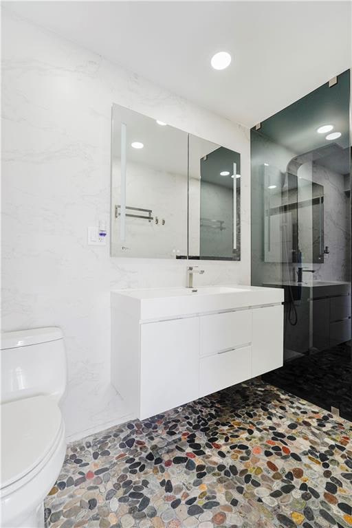 2546 E 13th St Unit A11, Brooklyn, NY 11235 - bathroom featuring toilet, vanity, walk in shower, stone finish flooring, and recessed lighting