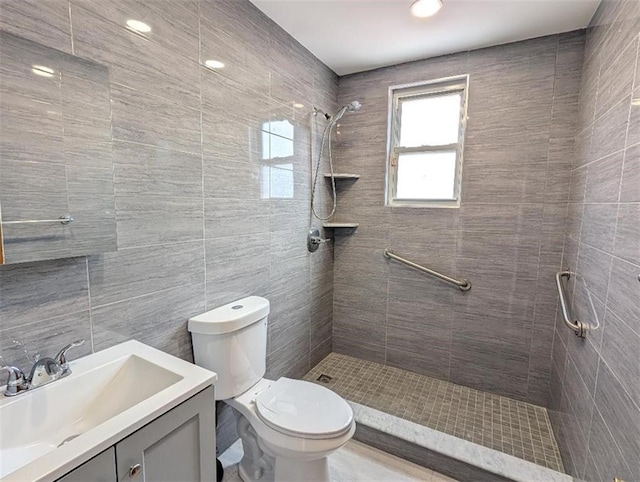 bathroom with a tile shower, vanity, tile walls, and toilet