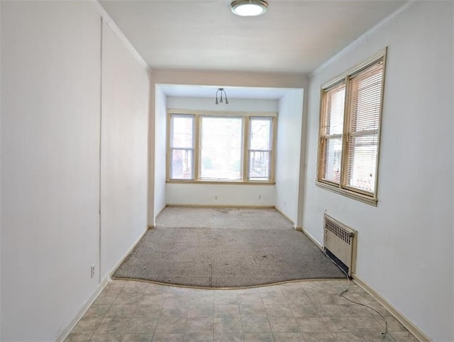 carpeted empty room featuring radiator, crown molding, and baseboards
