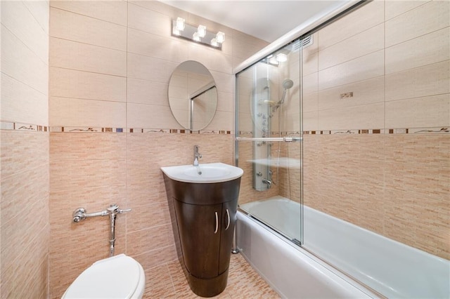bathroom with tile walls, enclosed tub / shower combo, toilet, and a sink
