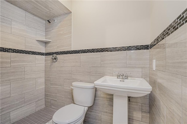 bathroom featuring tiled shower, toilet, tile walls, and wainscoting