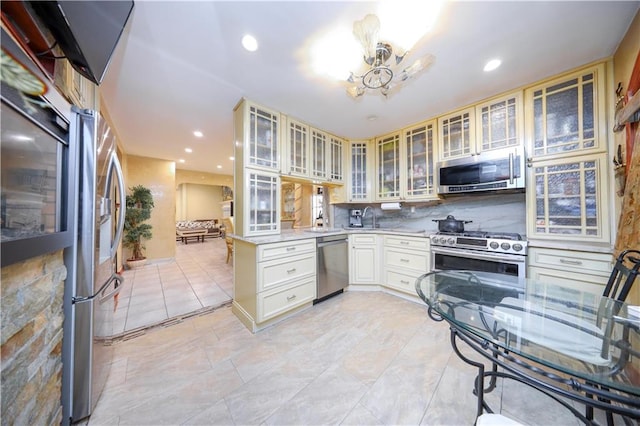 kitchen featuring appliances with stainless steel finishes, a peninsula, light countertops, glass insert cabinets, and a chandelier