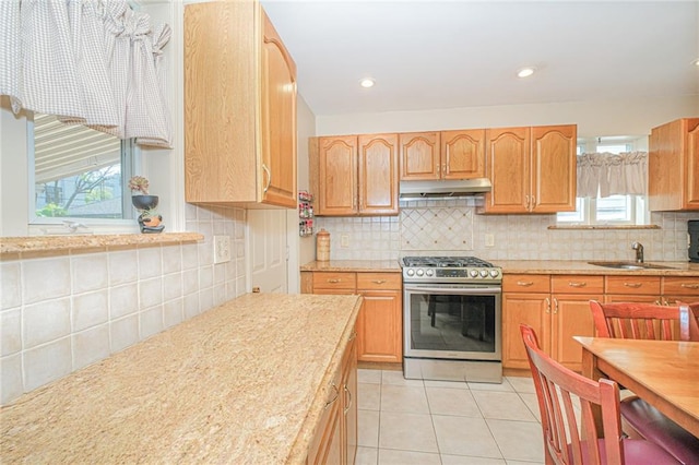 kitchen featuring stainless steel gas range oven, under cabinet range hood, a sink, and backsplash