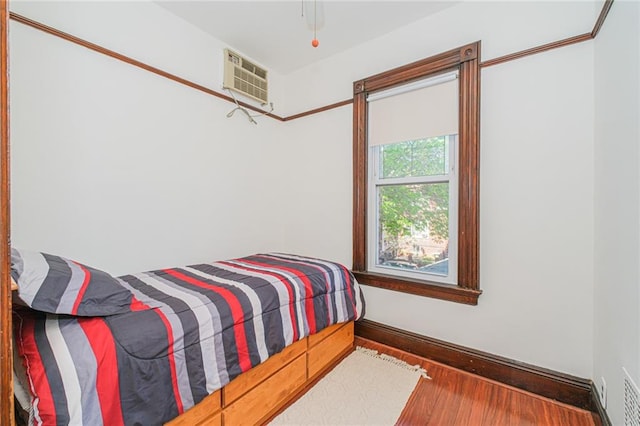 bedroom featuring wood finished floors, a wall unit AC, and baseboards