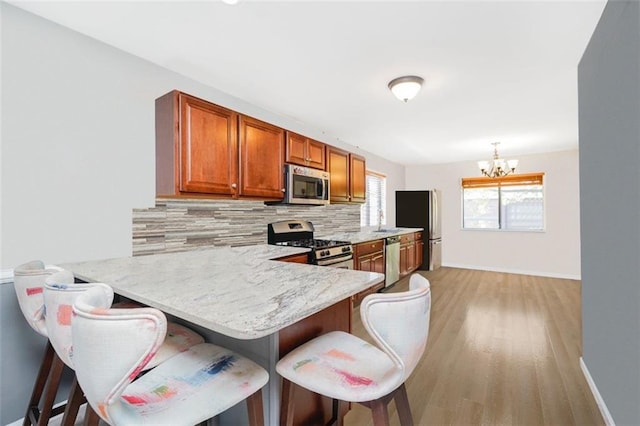 131 Stonegate Dr Unit 1, Staten Island, NY 10304 - kitchen featuring appliances with stainless steel finishes, a chandelier, backsplash, light wood-type flooring, and a kitchen bar