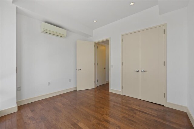 unfurnished bedroom with an AC wall unit, wood finished floors, baseboards, and recessed lighting