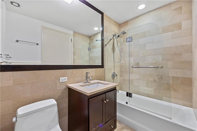 bathroom with bath / shower combo with glass door, toilet, vanity, tile walls, and recessed lighting