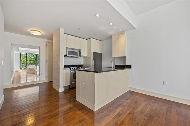 kitchen with stainless steel appliances, dark wood-style flooring, a peninsula, baseboards, and dark countertops